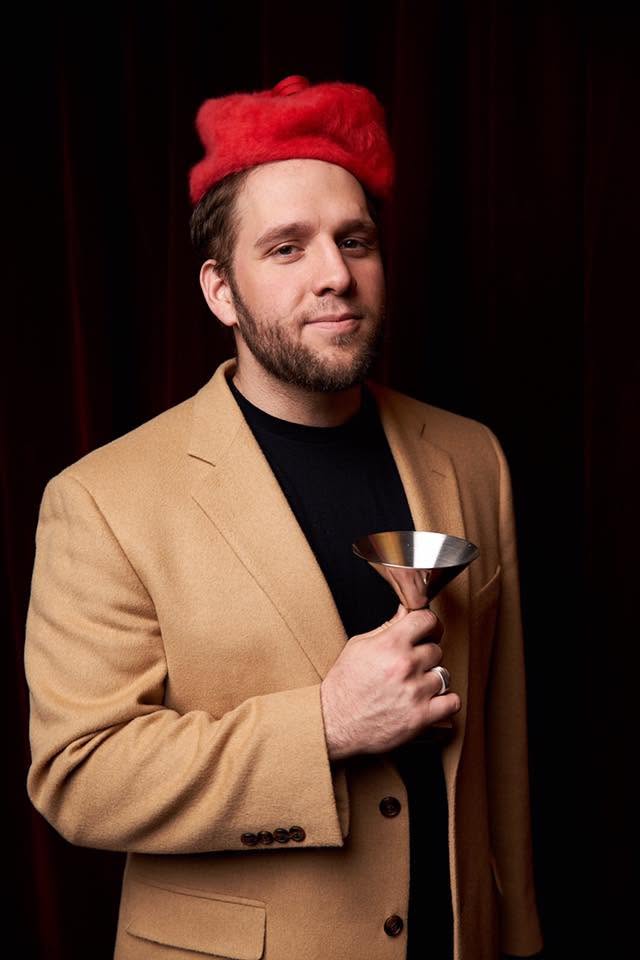 Brett Fink in a red hat and tan blazer, holding a martini glass